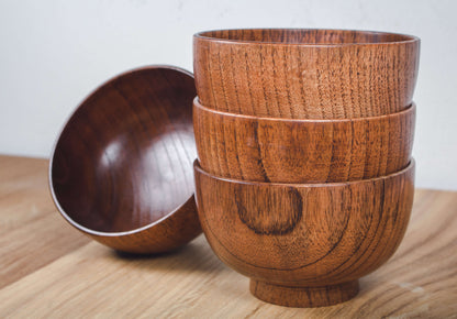 Eine Bowl aus Holz, von welcher die glatte Innenseite ersichtlich wird. Daneben befinden sich drei ineinander gestapelte Bowls mit gemaserter, individueller Außenseite.